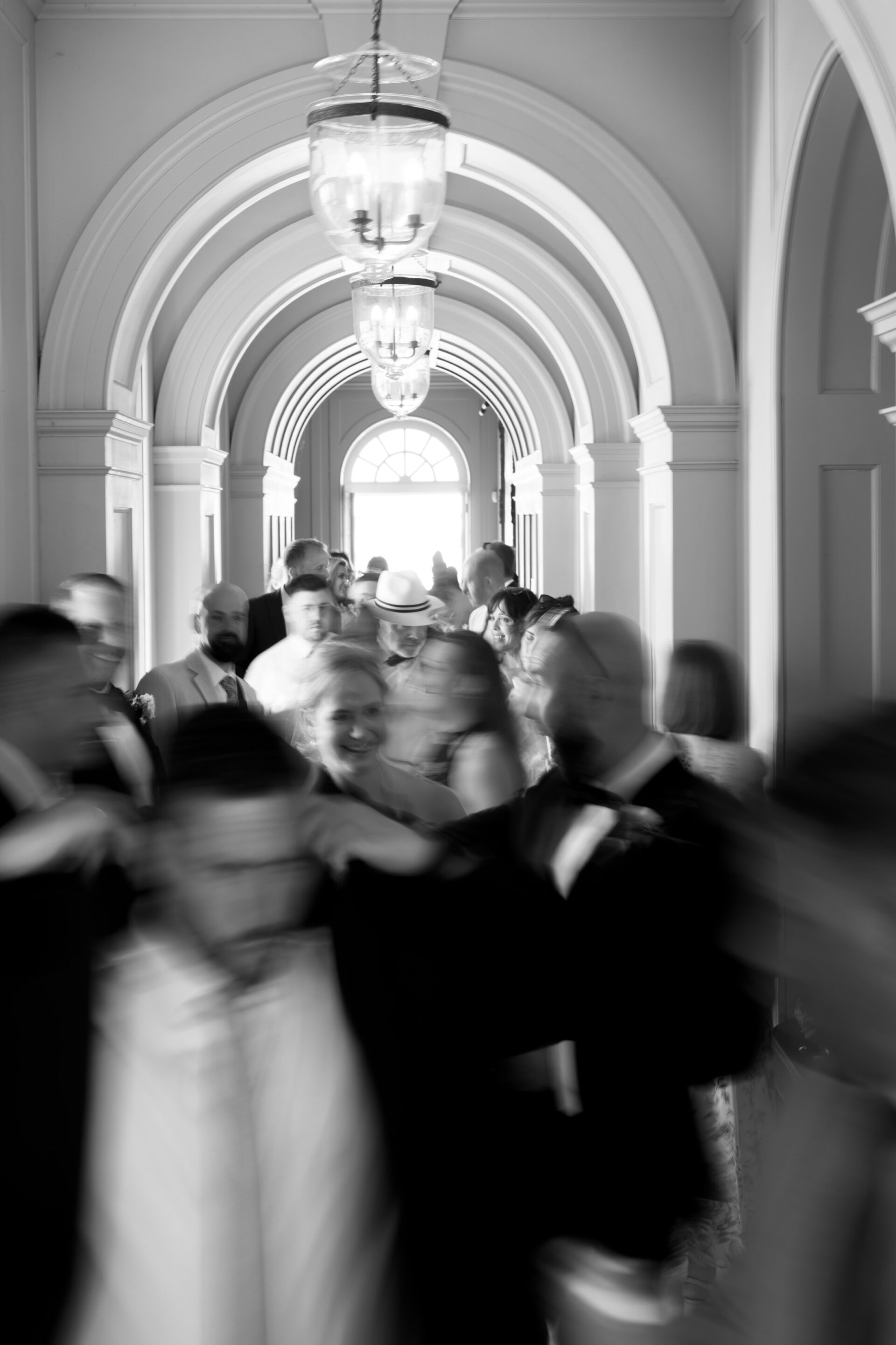 A black and white photo of people walking through an arched corridor, with a few of them looking blurry because they're moving.