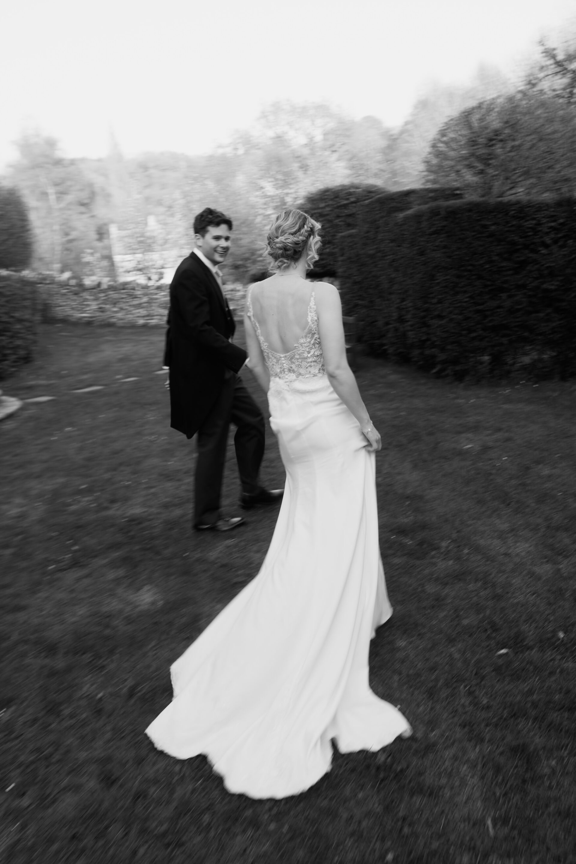A bride in a white dress and a man in a suit walk on the grass; the photo is black and white and a bit blurry.