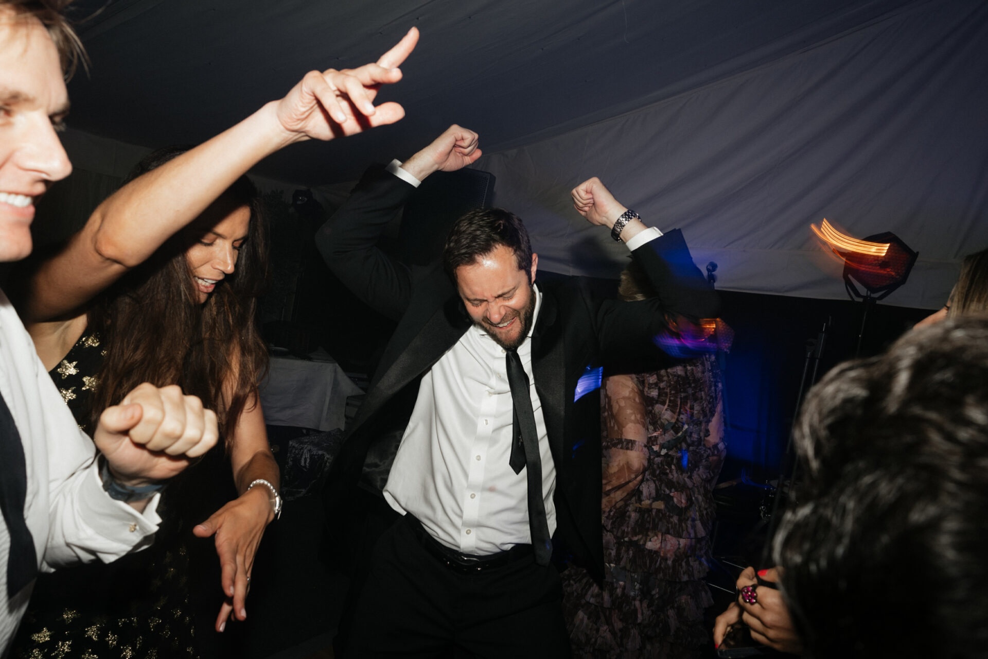 People dressed up in nice clothes dance with lots of energy at an indoor party with low lighting.