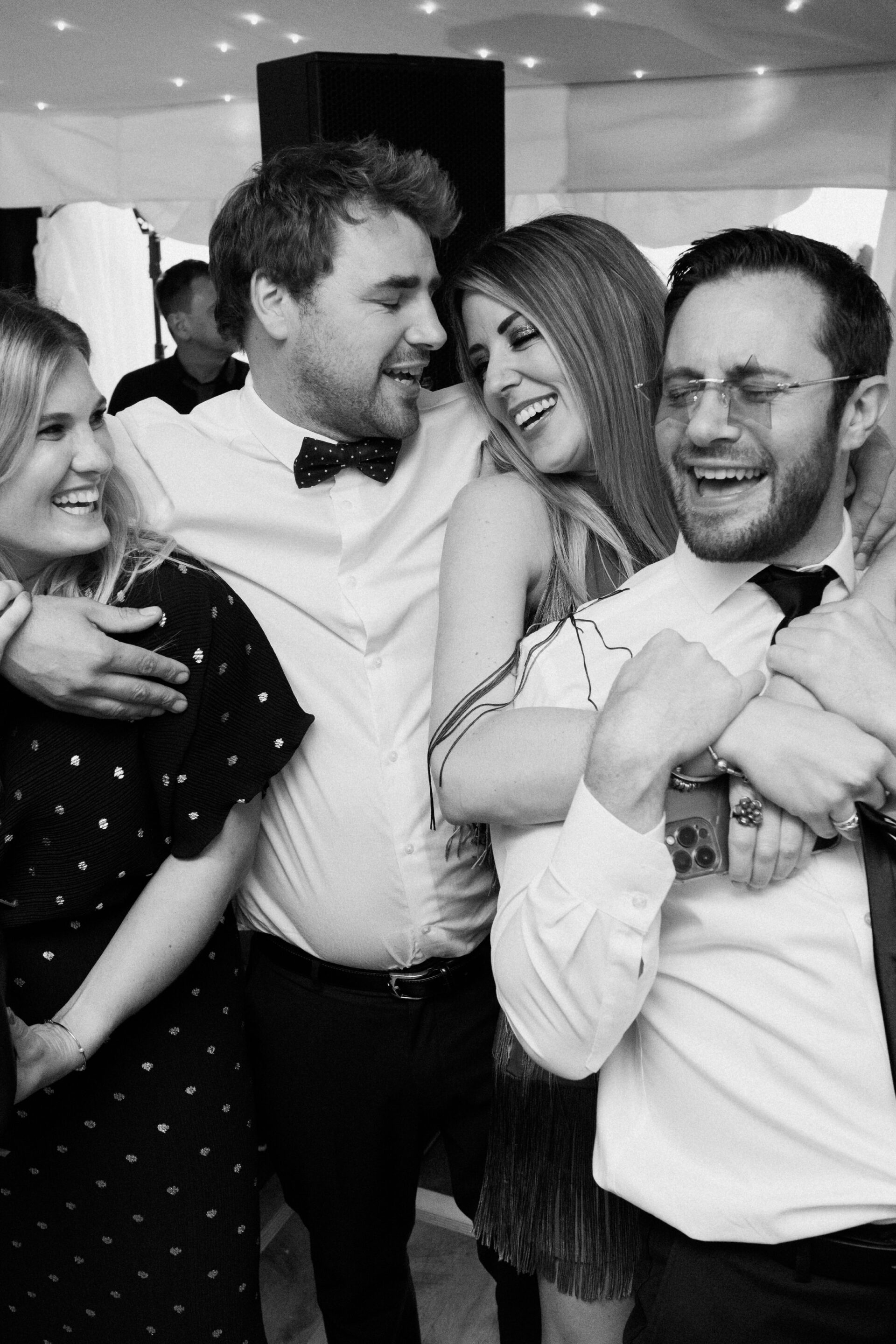 Four adults dressed up, smiling and laughing together as they pose for a group photo at an inside event.