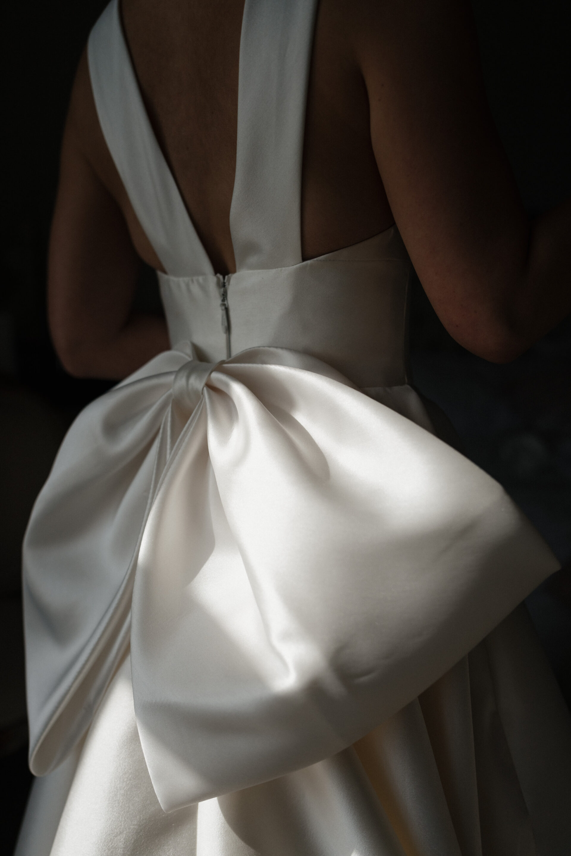 Someone in a white dress with a big bow on the back is seen from behind under gentle lighting.