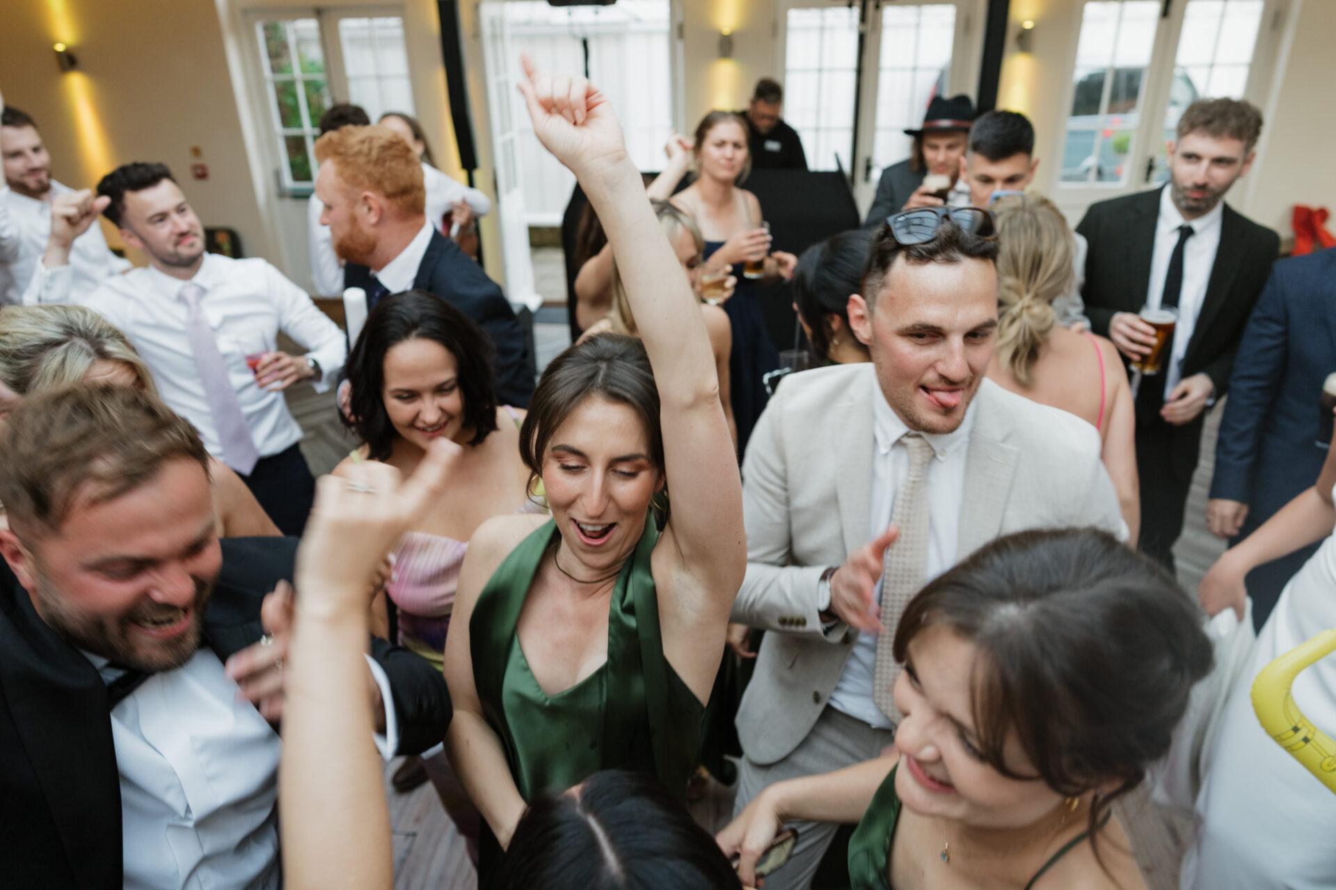 People dressed up are dancing and having fun inside, with a woman in the middle lifting her arm.