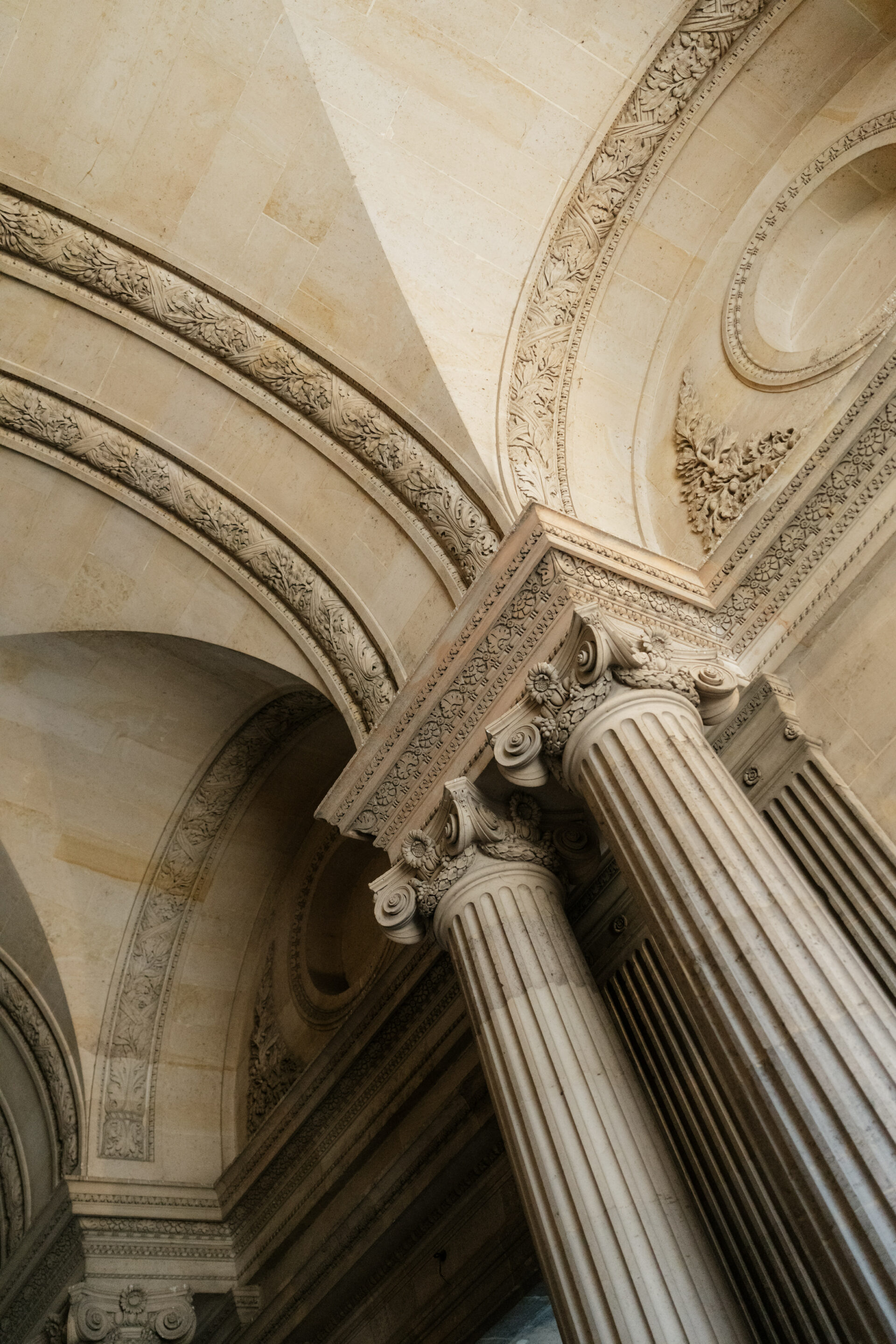 Tall stone columns with fancy tops hold up arched ceilings covered in detailed carvings and patterns in a classic style.