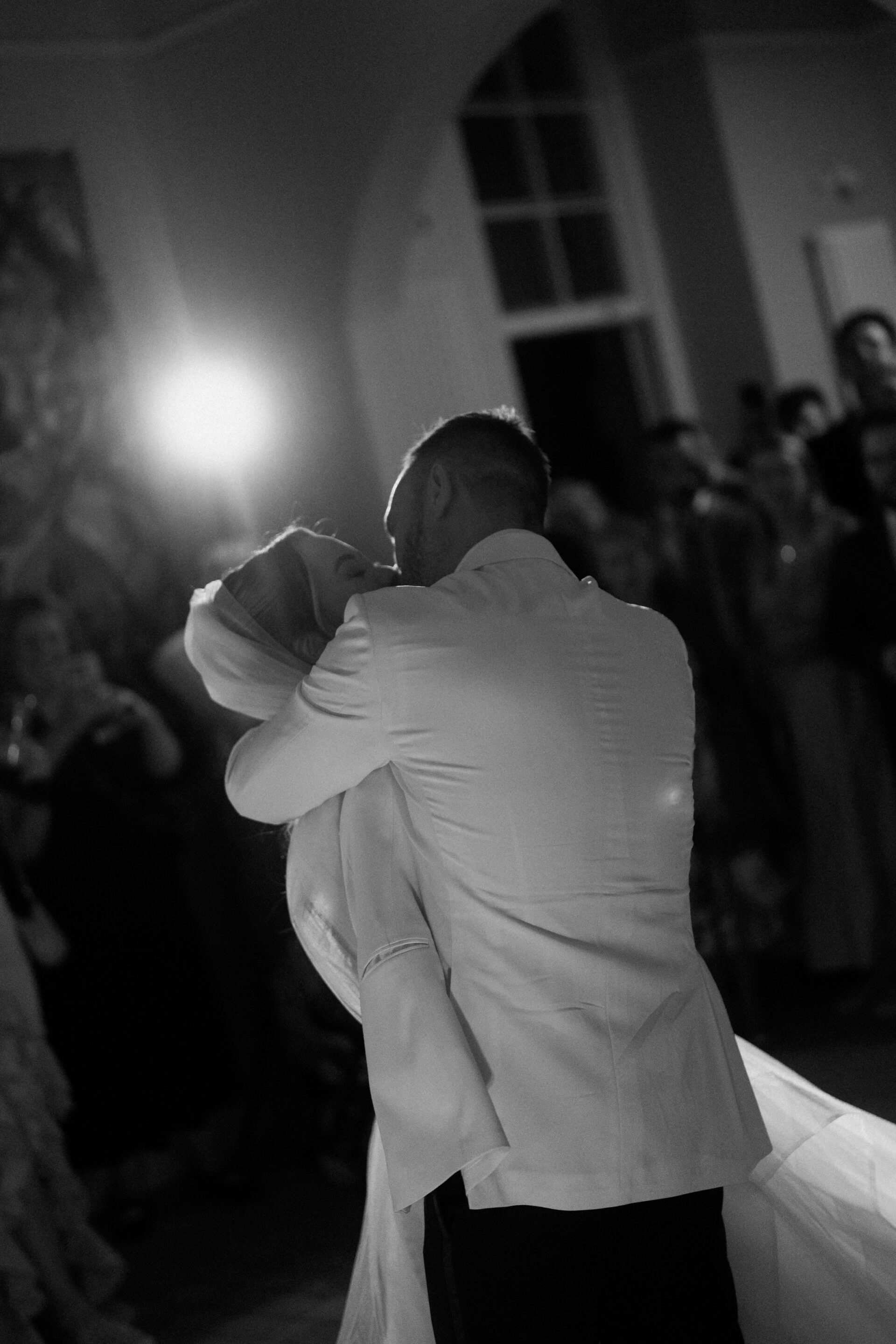 A bride and groom dance closely together at their indoor reception while guests watch in the background.
