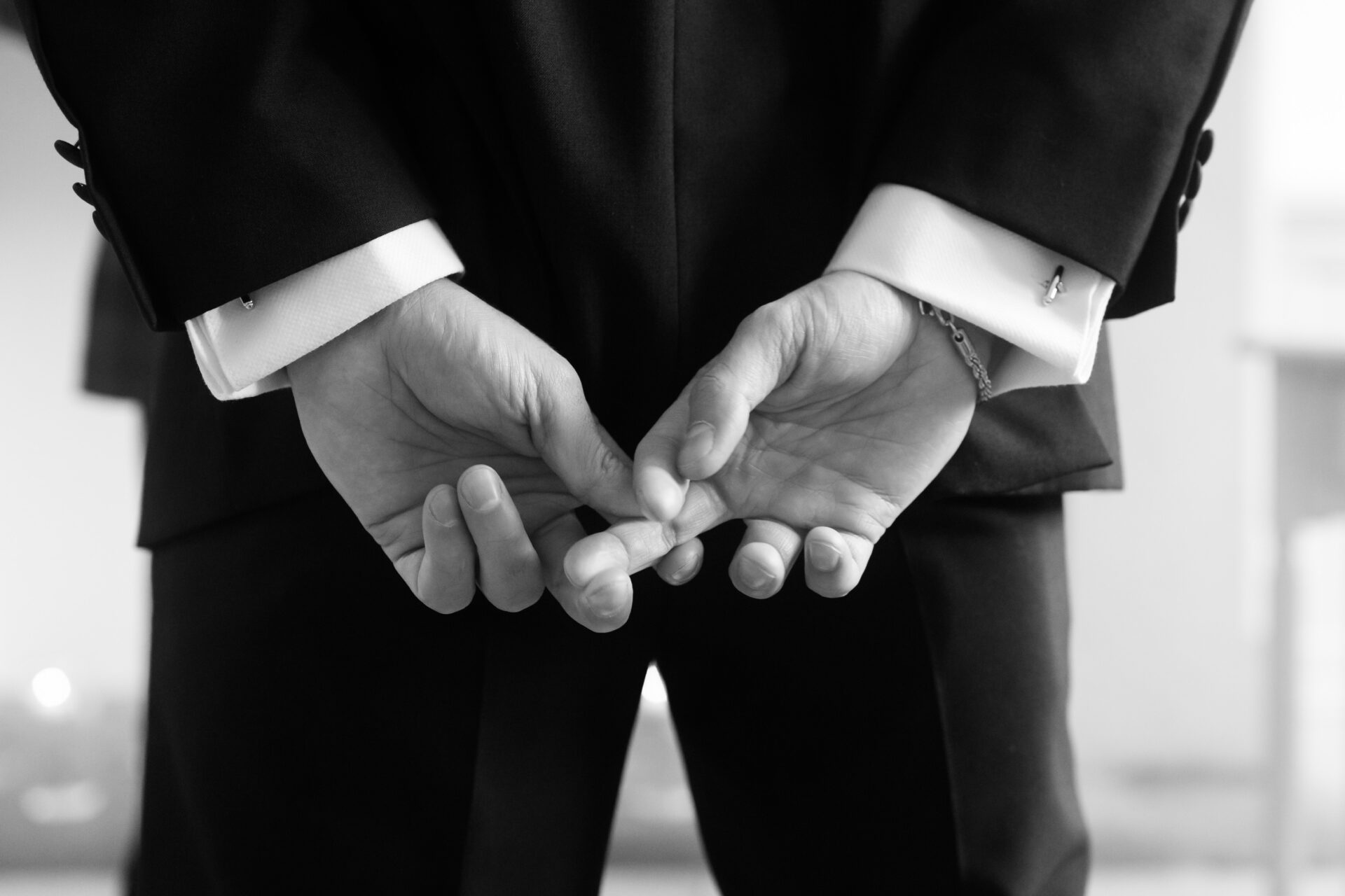 Someone wearing a suit is standing with their hands held together behind them.