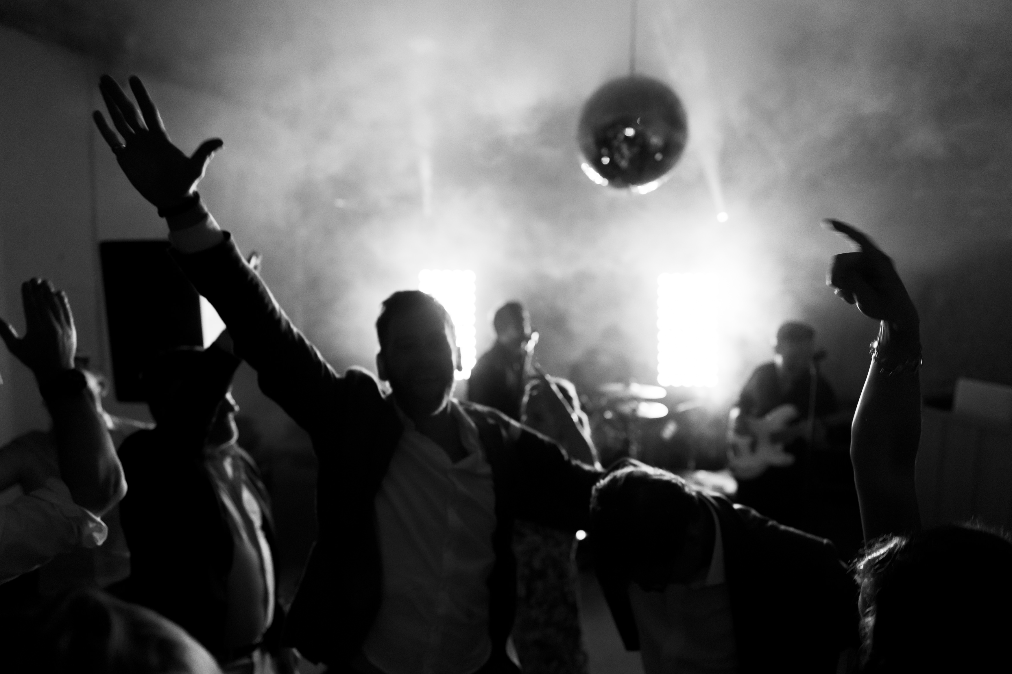 A black and white photo shows people dancing energetically under a disco ball with bright lights and fog, creating a lively party vibe.