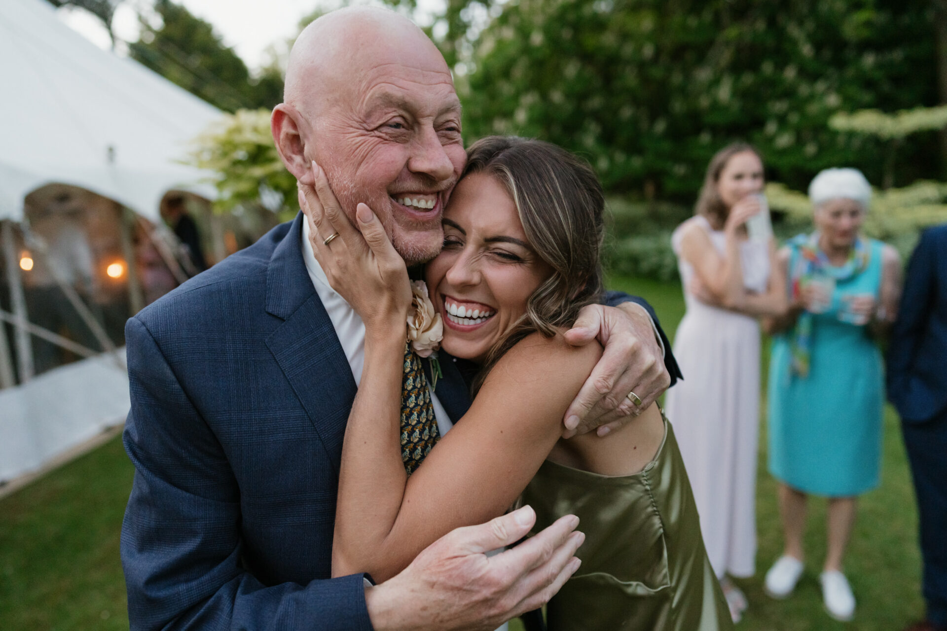 A woman wearing a green dress is hugging a man in a suit, who is smiling. They are outside at an event, and you can see three other people in the background.
