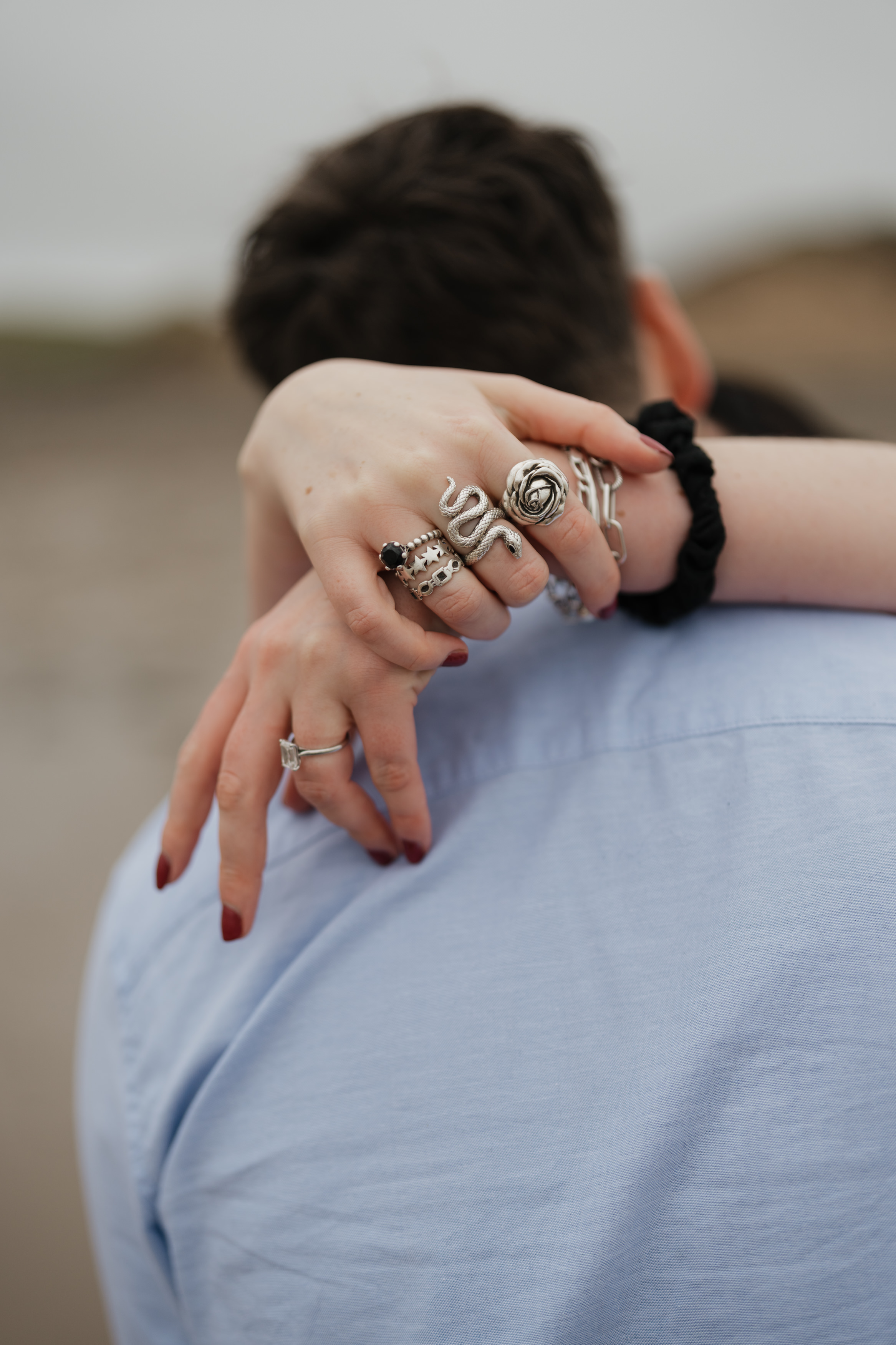 A person is hugging another from behind, with their hands on the other person's shoulders, and you can see that they're wearing several rings.