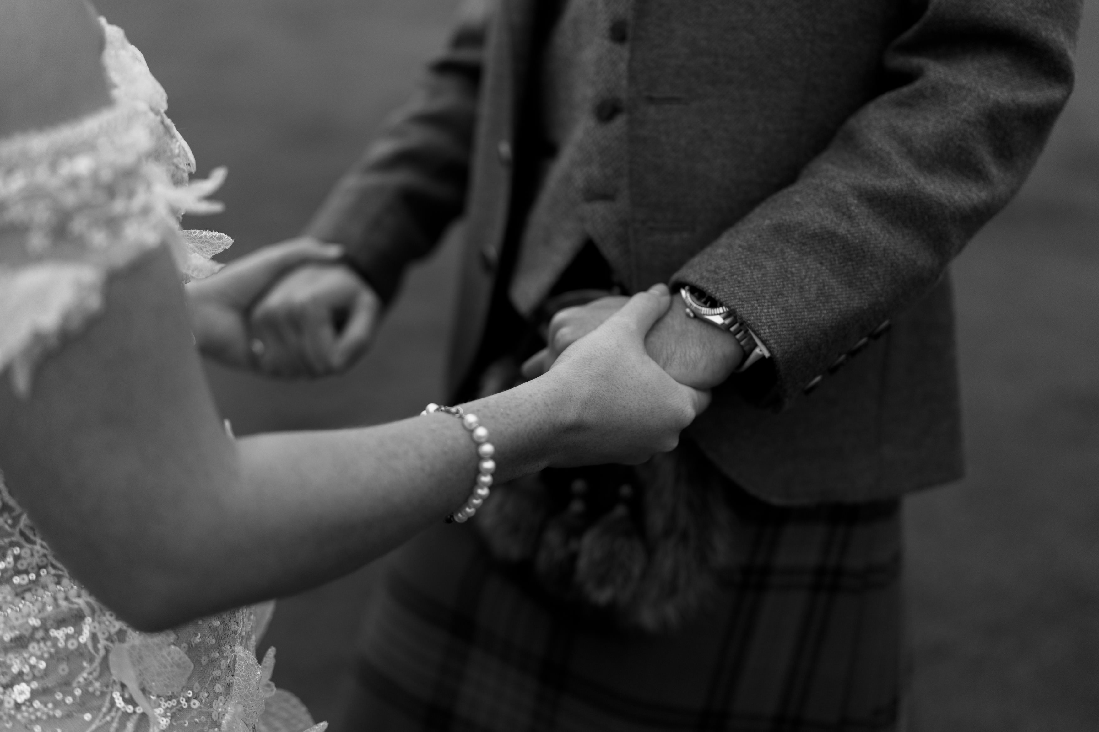 Two people wearing fancy clothes are holding hands, and one of them is wearing a kilt. The photo is in black and white.