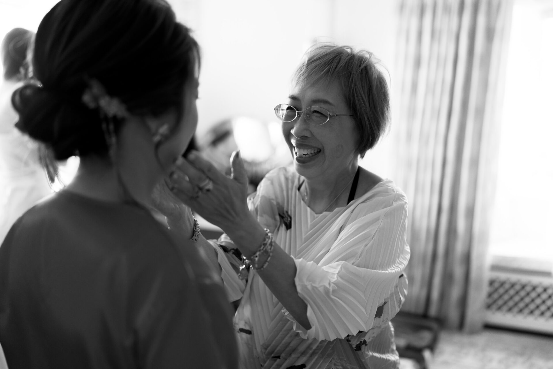 An older woman is smiling and gently touching a younger woman's face in a warmly lit room.
