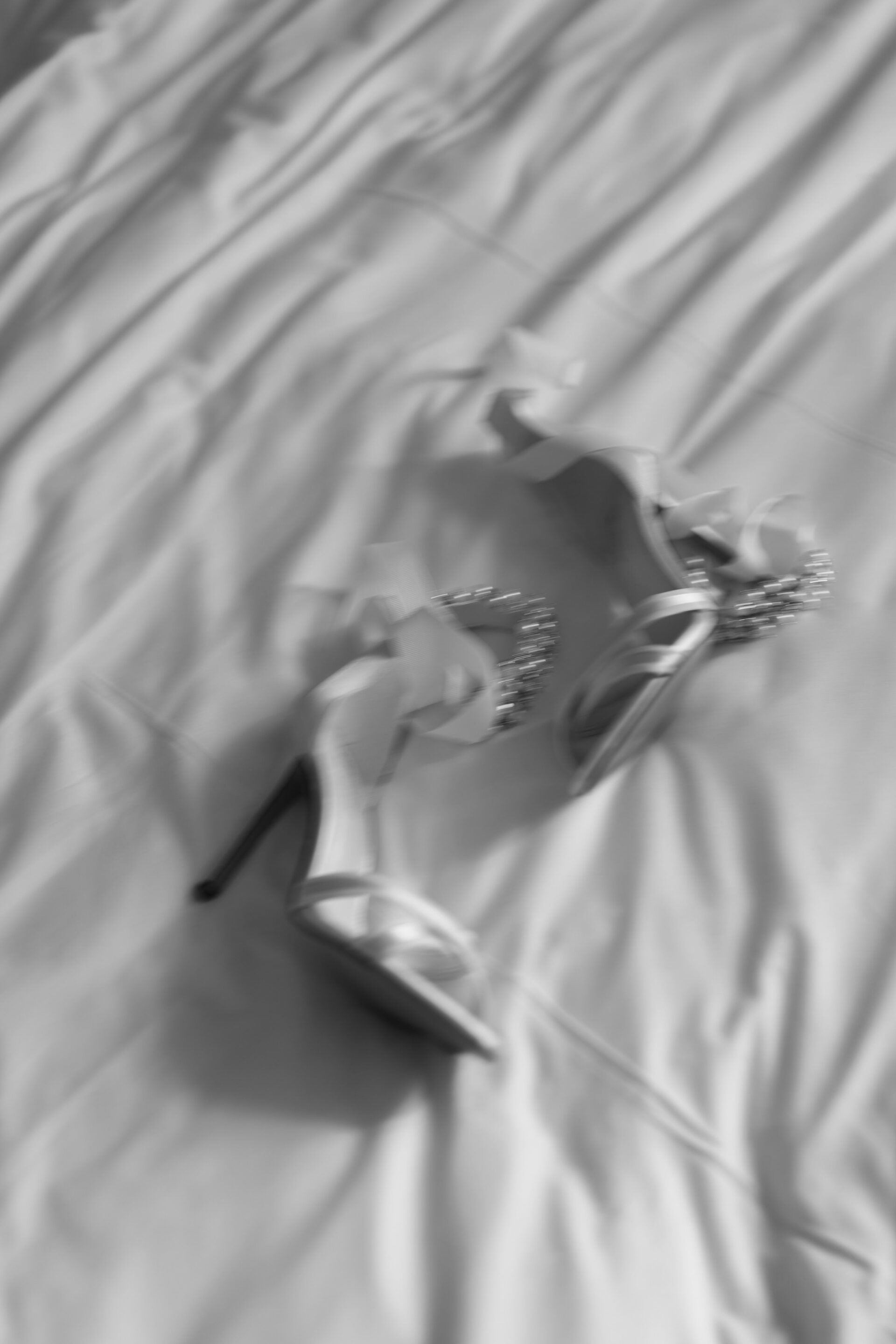 A pair of high-heeled sandals with decorative designs lying on a wrinkled, light fabric.