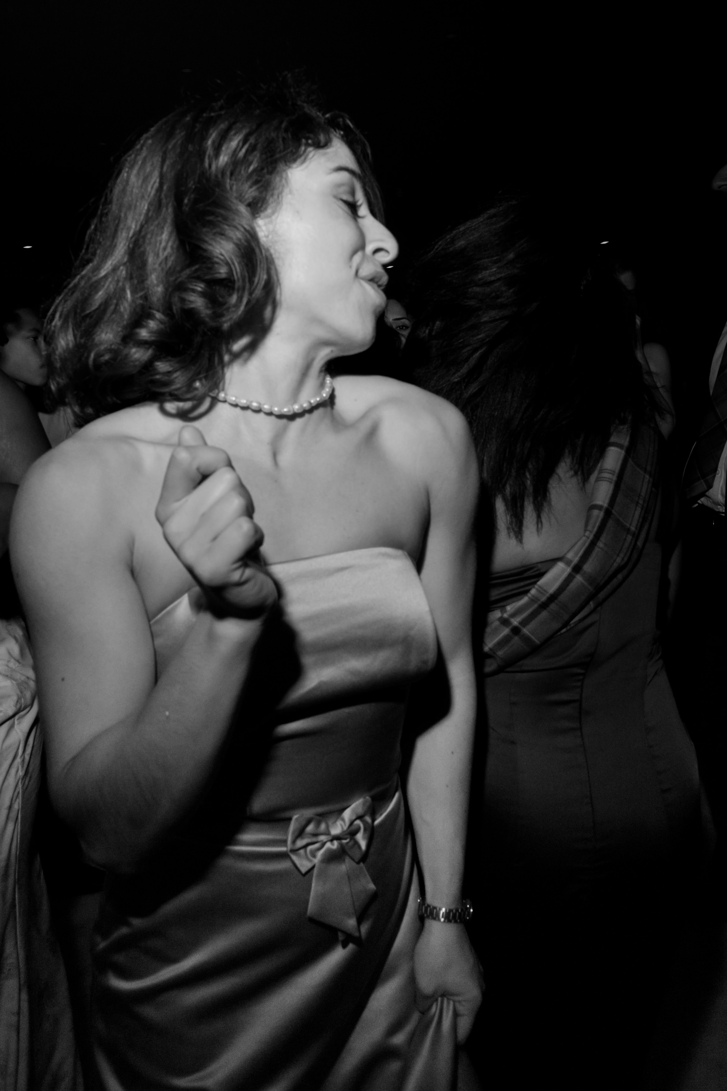 A woman in a strapless dress is dancing with lots of energy in a place that's not very well lit.