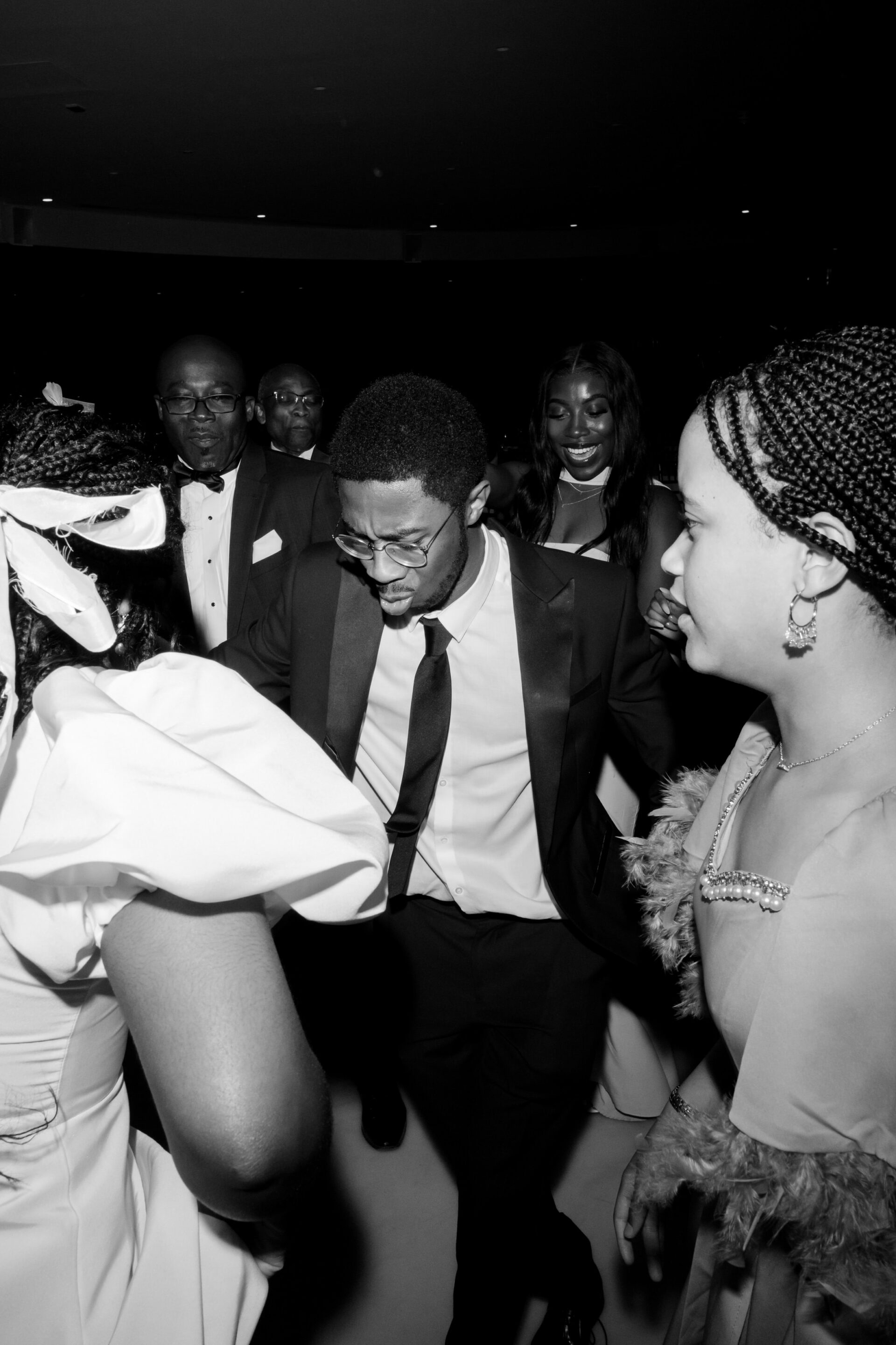 A bunch of people in fancy clothes are dancing and chatting in a room with low lighting.